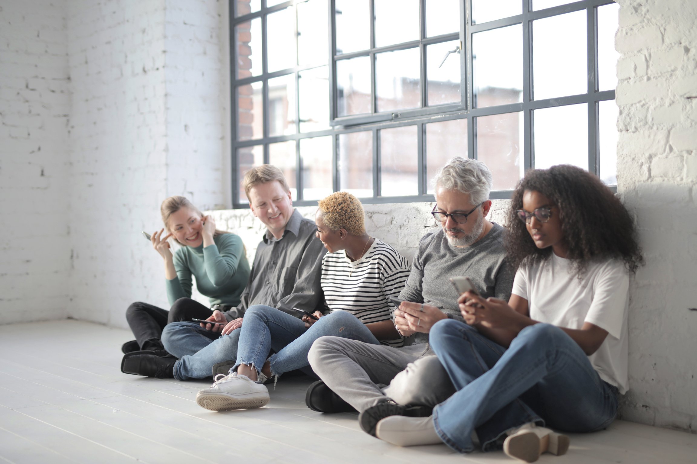 Happy multiracial colleagues sitting on social media using smartphones